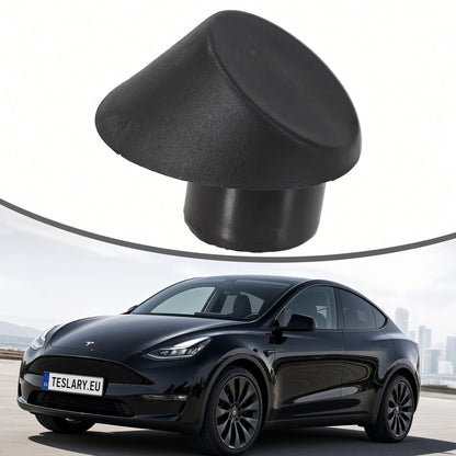 A black rubber or foam dome-shaped cap or plug shown above a black Tesla Model Y on a road with a city skyline in the background. The product appears to be the black cap, with the car used as contextual imagery rather than the product itself. Tesla Trunk Rubber Stopper 1507940-00-C and 1507942-00-C Buy from Ireland and Europes teslary.eu